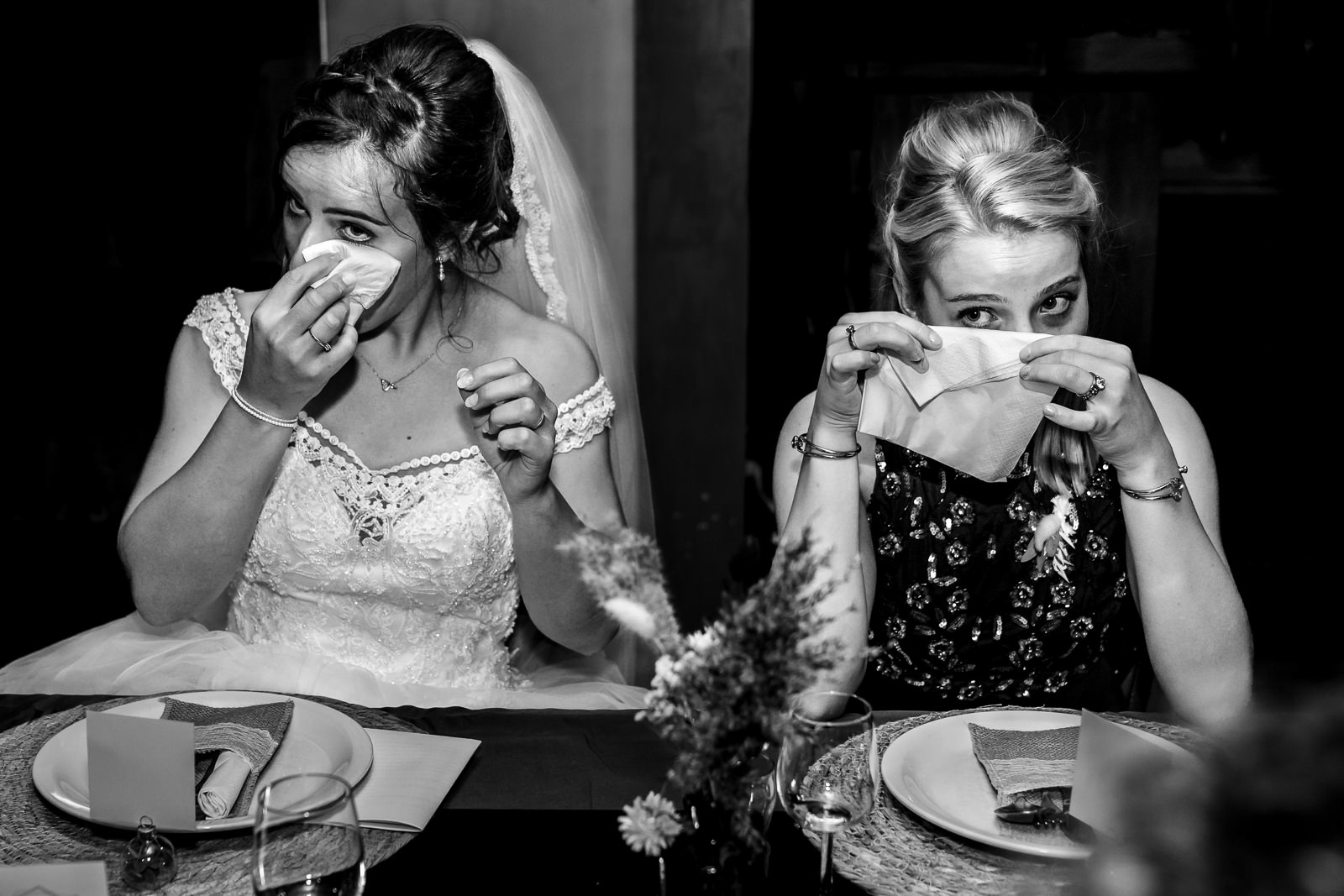 Verhalende trouwfotografie: vader van de bruid spreekt tijdens het diner terwijl de bruid en haar zus tranen wegvegen met een zakdoek.