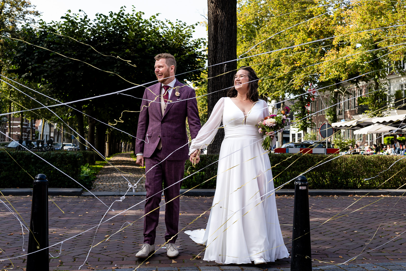 Bruid en bruidegom lopen door confetti tijdens hun aankomst bij het gemeentehuis in Oisterwijk bij het Trouwlaantje.