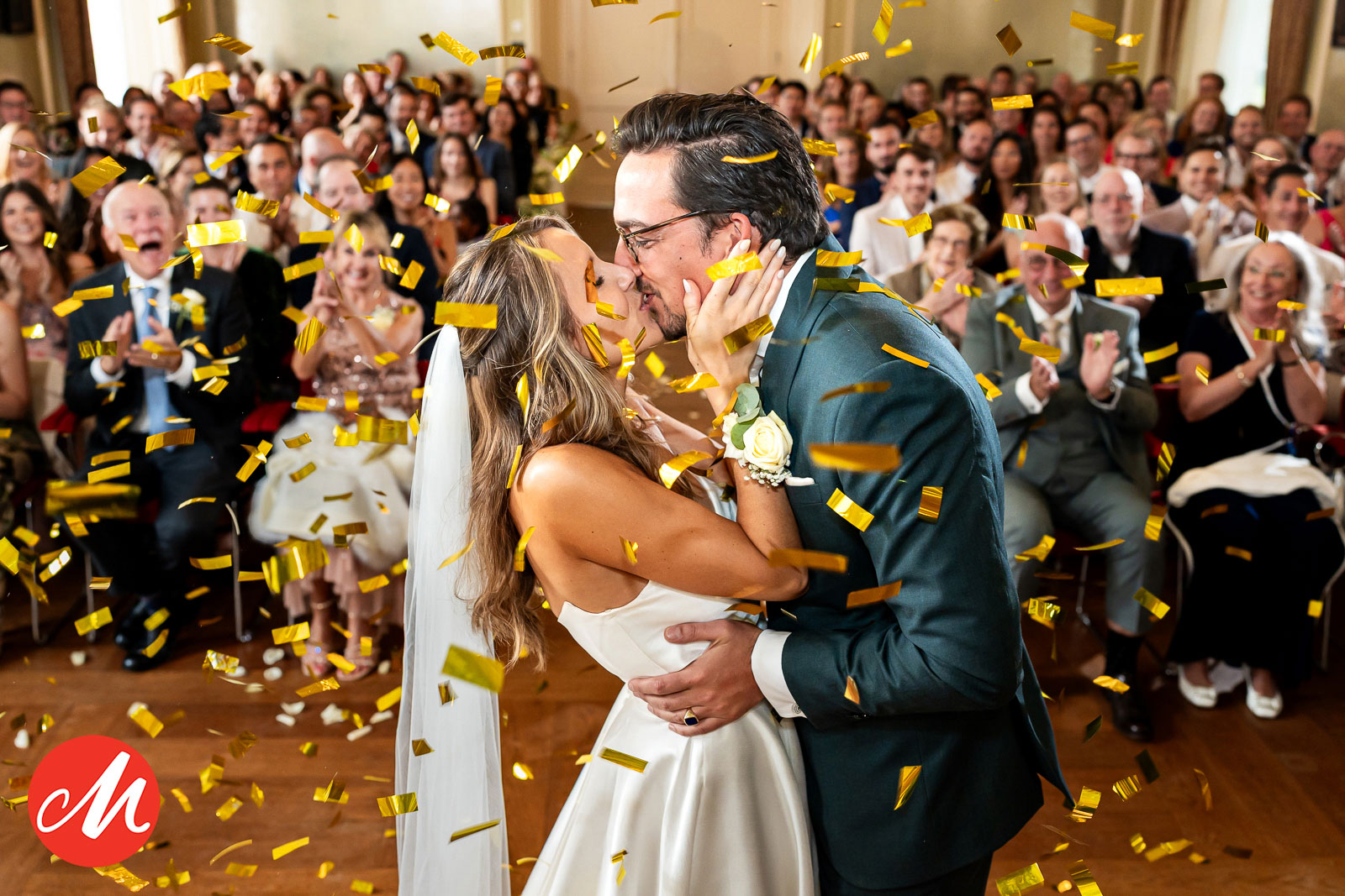 Bruid en bruidegom kussen elkaar na het ja-woord tijdens de ceremonie met confetti en enthousiaste gasten.